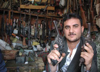 An arms merchant displays two old British revolvers, while modern Russian weapons hang on the wall of his shop.