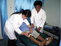 Dr. Jo Jong Gill and Nurse Hwang Un Ha using electrical acupuncture to create localized electrical pulses in the leg muscles to encourage free blood flow to key areas in the body.